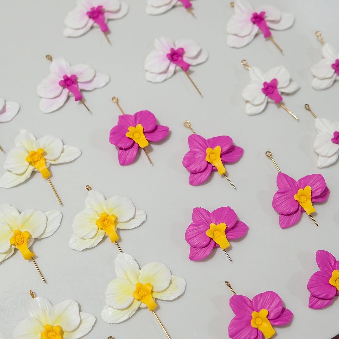 Rows of hand-sculpted orchid clay pieces laid out on a production table, waiting to be assembled into finished earrings