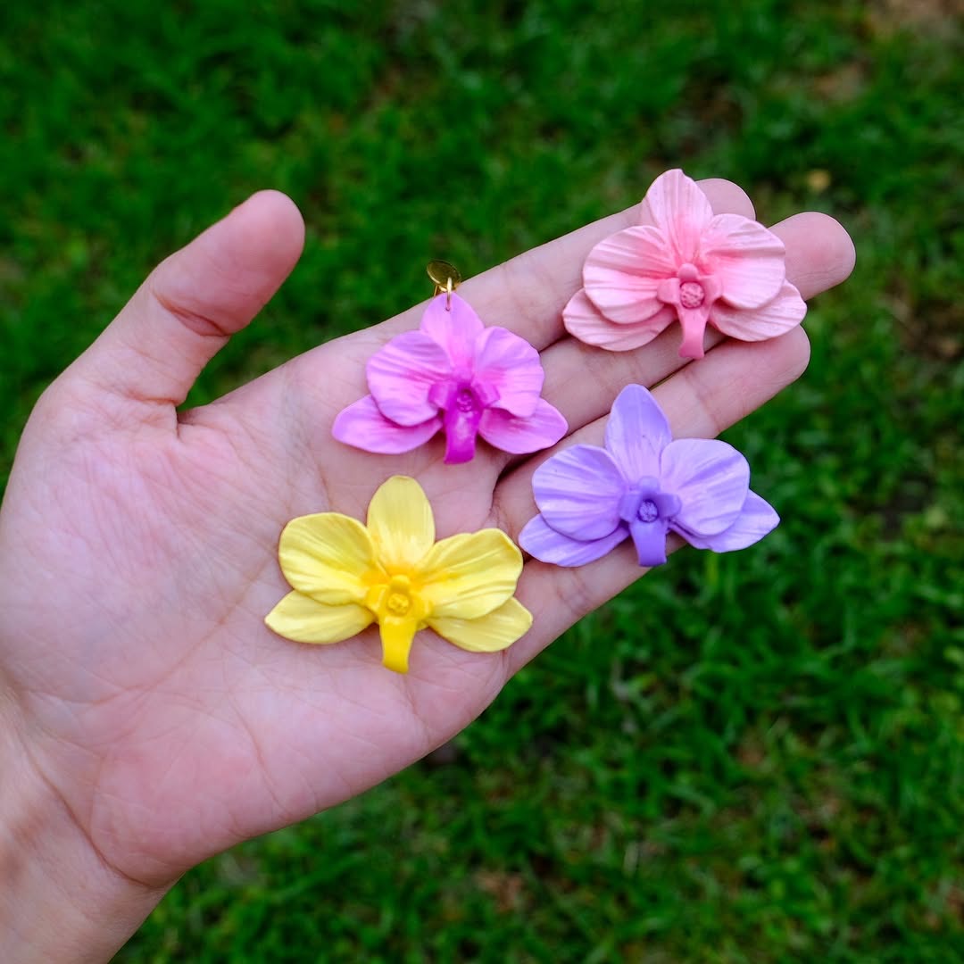 Four orchid clay charms in hand — pink, magenta, yellow and purple