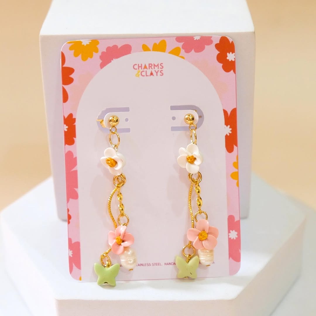 Pastel floral earrings close-up — pink cherry blossom and green butterfly clay pieces